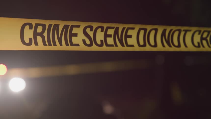 A person moves in front of a spotlight that illuminates an area closed off with crime scene tape