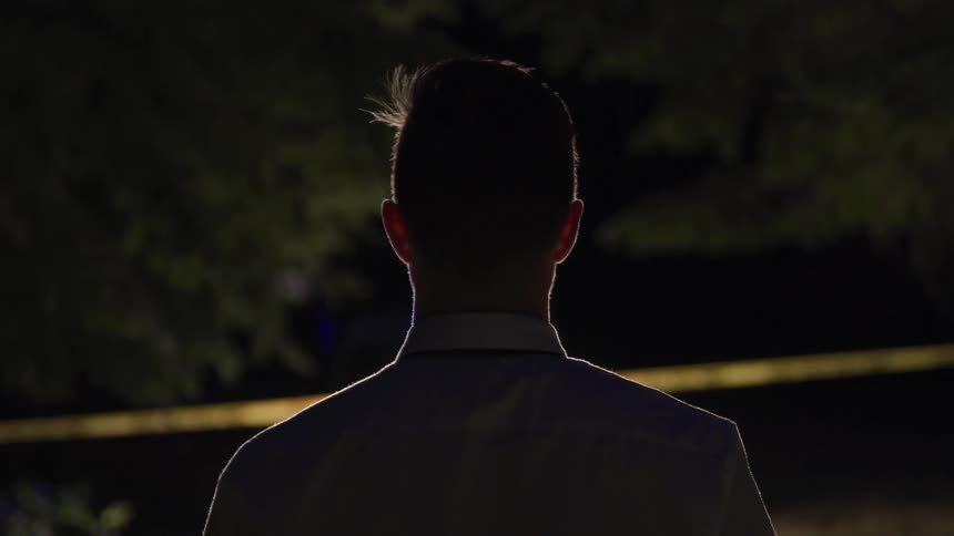 A man is standing behind the tape near a crime scene