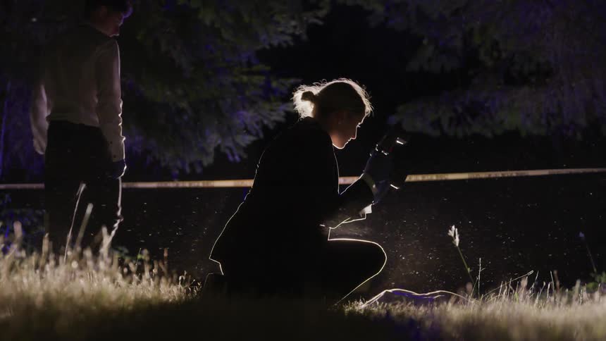 A woman photographs something while a man walks past