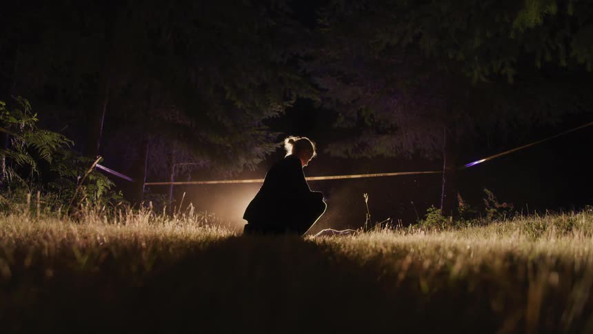 A woman kneels in a field surrounded by crime scene tape