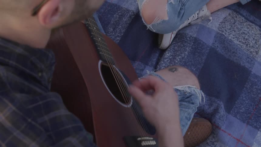 A young man plays the guitar as he sits with another person