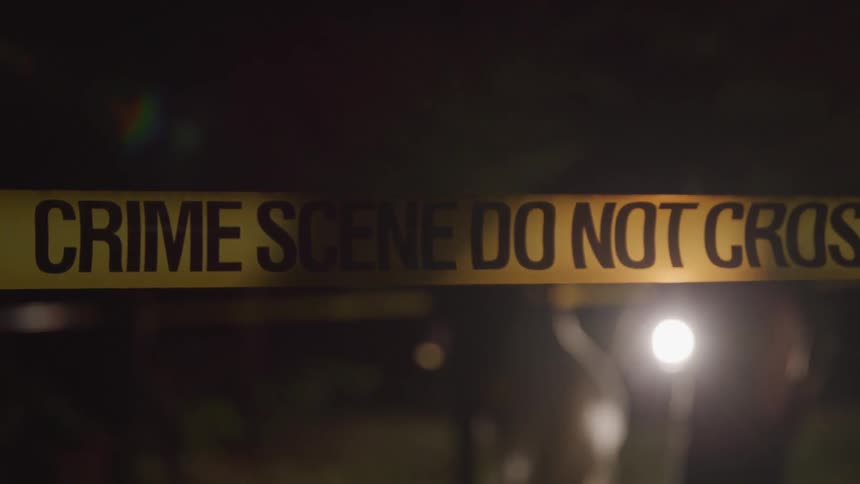 Two people are seen walking behind an area closed off with crime scene tape