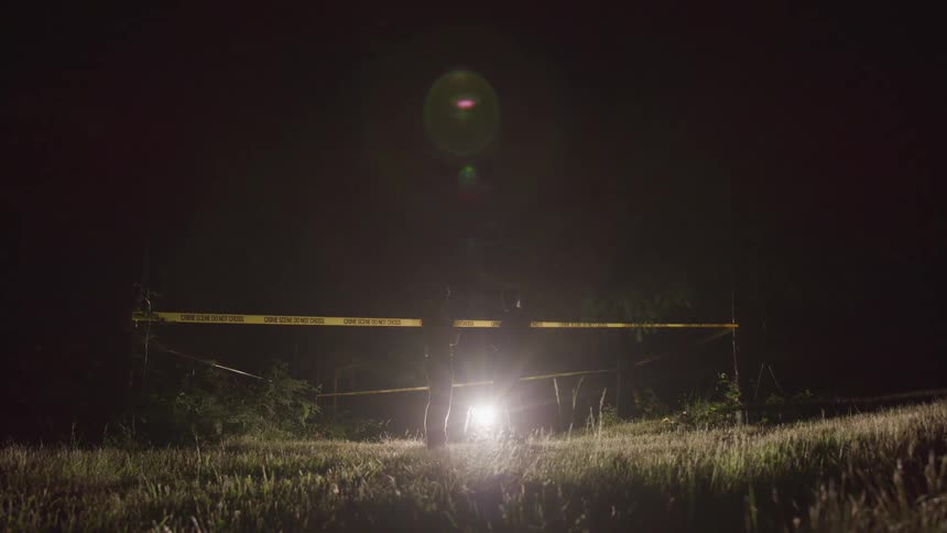Two police officers talk in front of crime scene tape at night