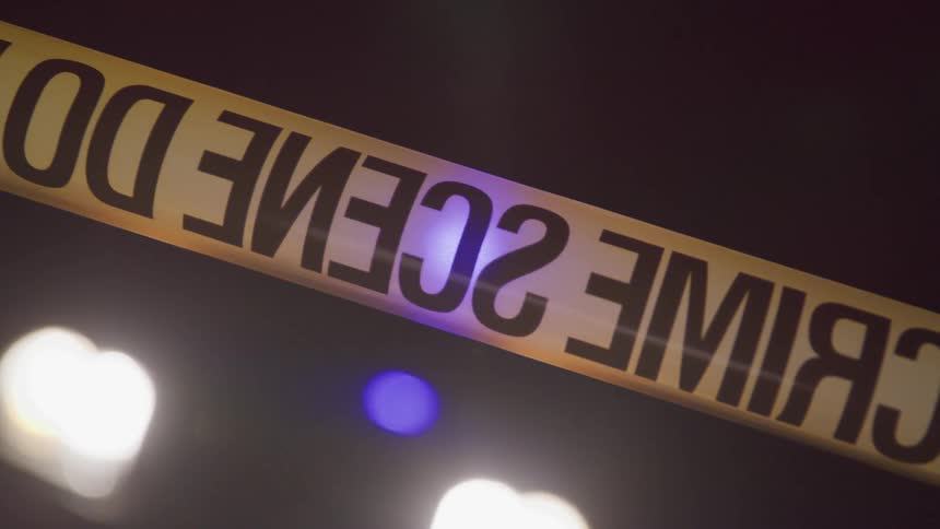 Close up of crime scene tape with flashing lights behind