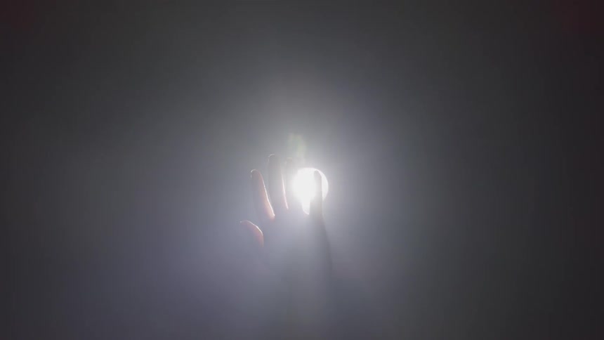 A persons hand waving in front of a light bulb