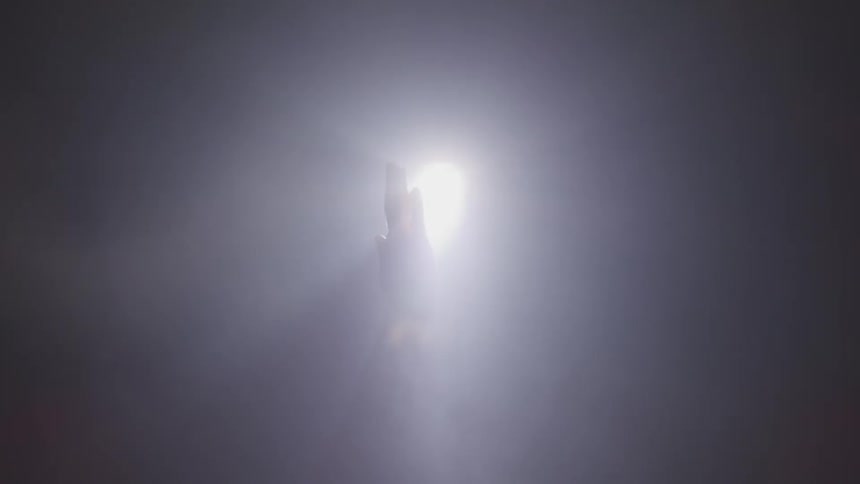 A persons hand in front of a light with smoke and flair