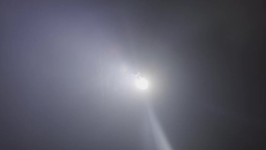 The silhouette of a hand holding a gun in a beam of light at night
