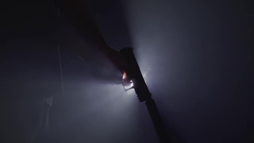 Close up of a person pointing a gun with a bright light in the background