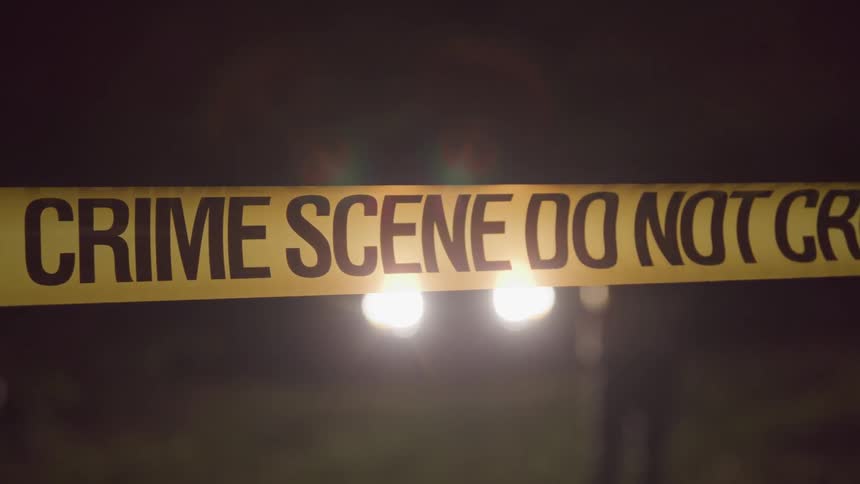 Close up of crime scene tape with people walking behind it