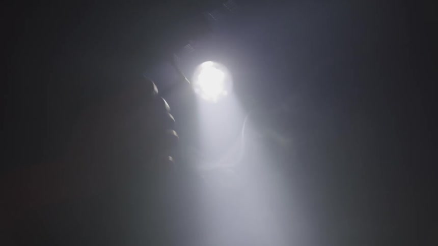 The silhouette of a handgun with a silencer on it can be seen firing in front of a bright light