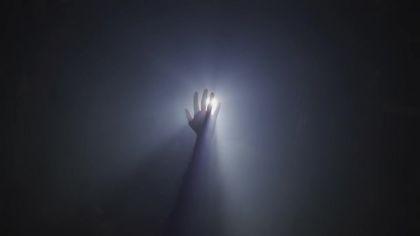 Person holds hands in spotlight in dark room