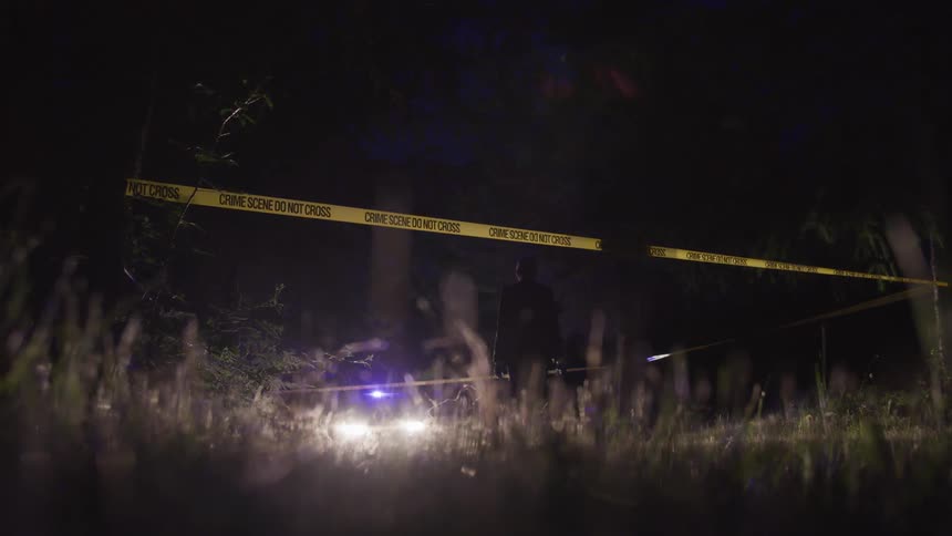 An area of a field sectioned off with crime scene tape while people investigate