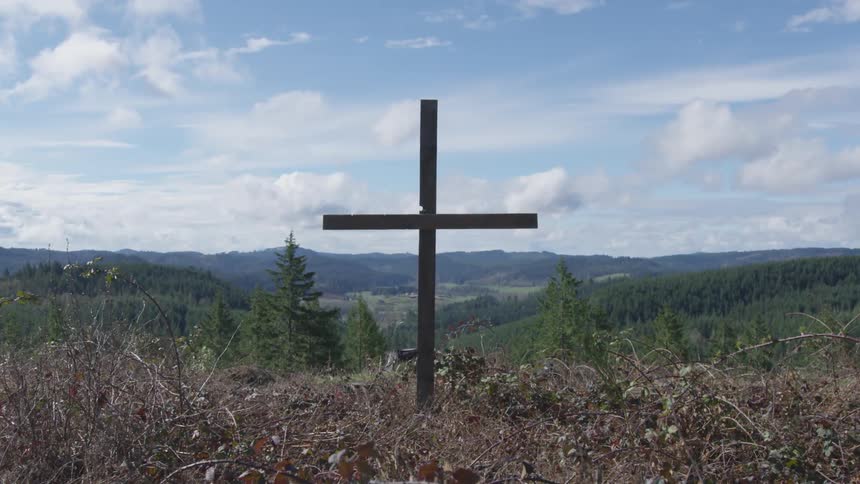 Wooden cross stands with mountain range valley and forest in background