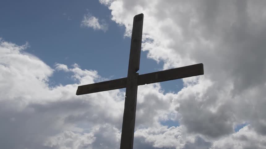 A wooden cross against a blue sky with white clouds