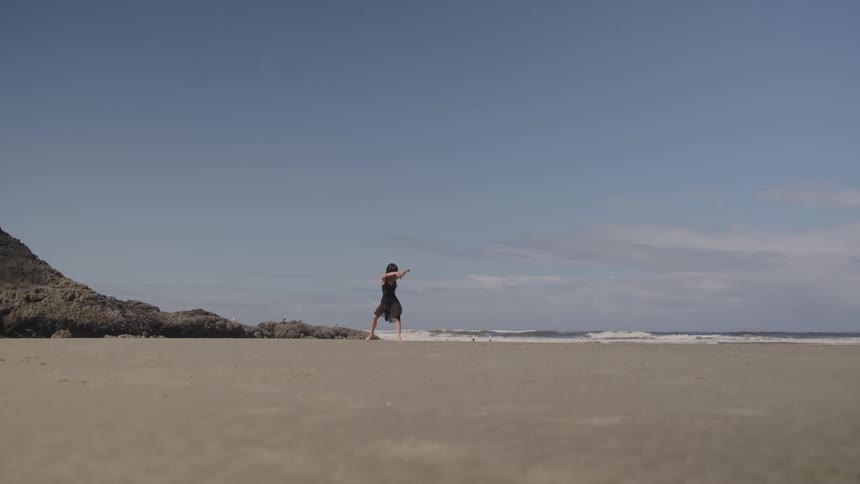 Asian woman in black dress dances on the sand beach next to the sea
