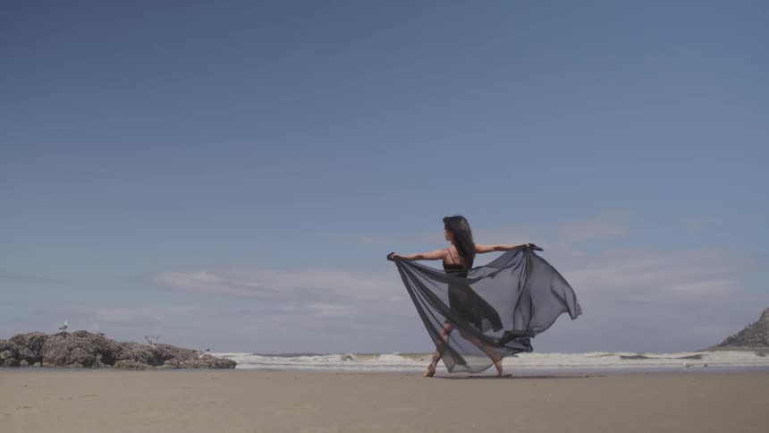 A young asian woman dances on a beach