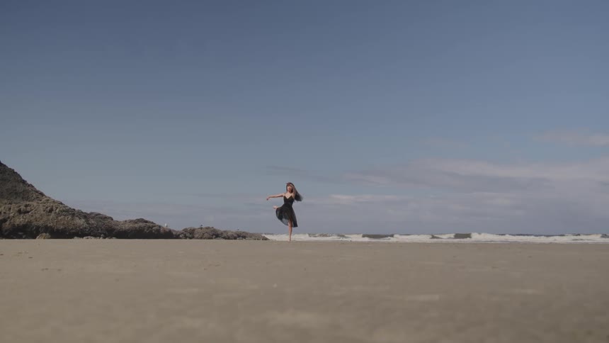 A woman in a black shawl dancing on the beach