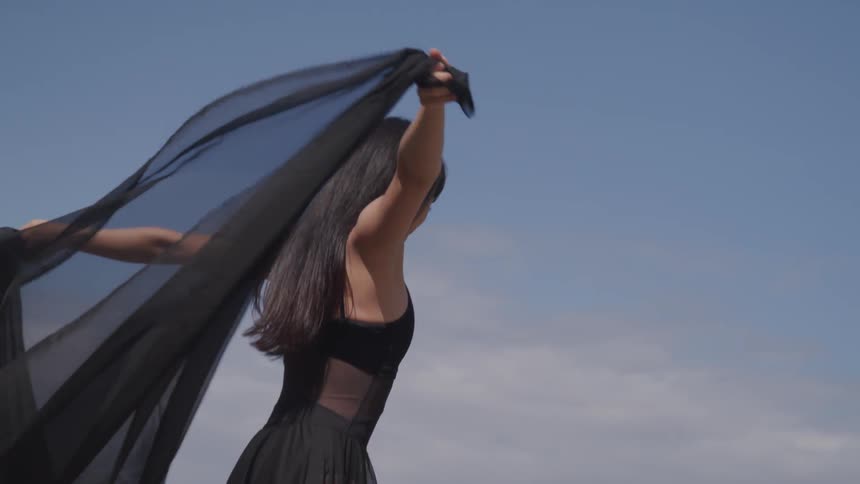An asian woman dressed in black performs a dance on a beach