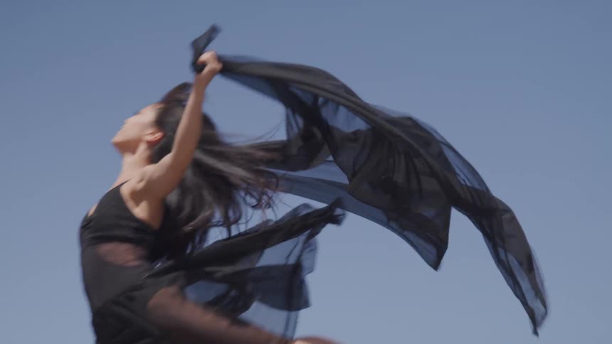 An asian woman in black clothing leaps through the air
