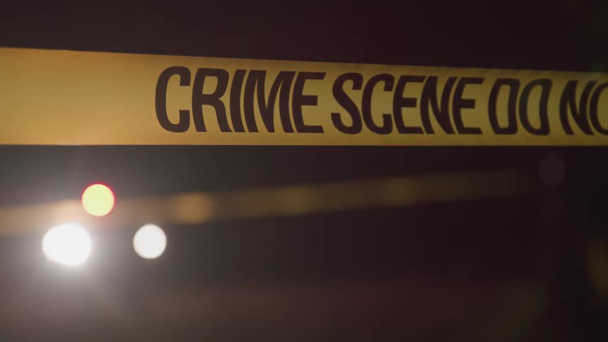 A person walking towards a police car ducking under a crime scene tape
