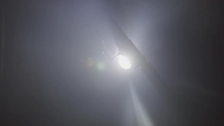 The silhouette of a pistol with a silencer being fired downward is seen in front of a bright light