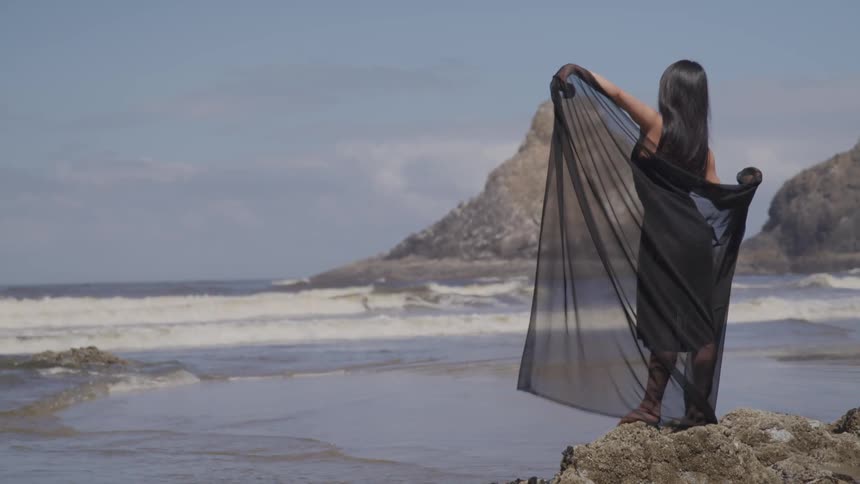 A woman in a black shawl dancing on the beach