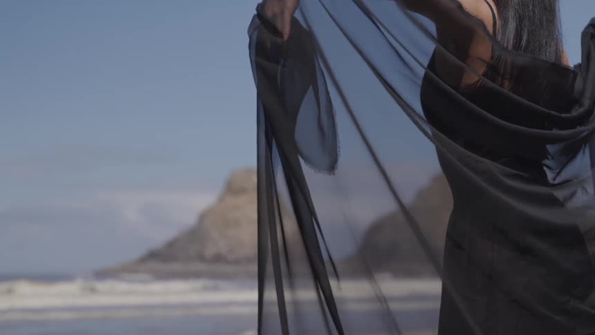 A woman in a black shawl dancing on the beach
