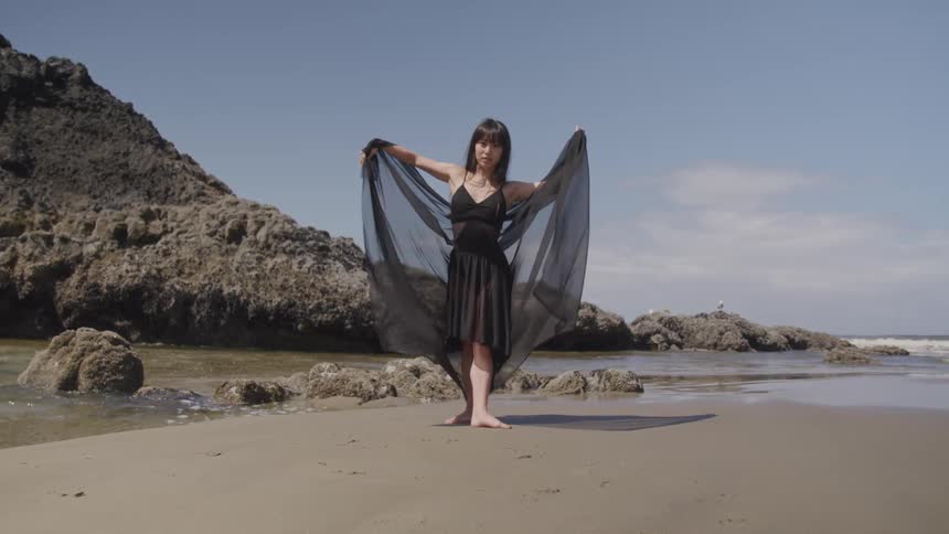 A woman in a black shawl dancing on the beach