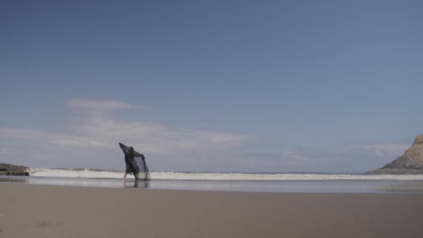 A female dancer is dancing on a beach holding a large piece of black sheer fabric