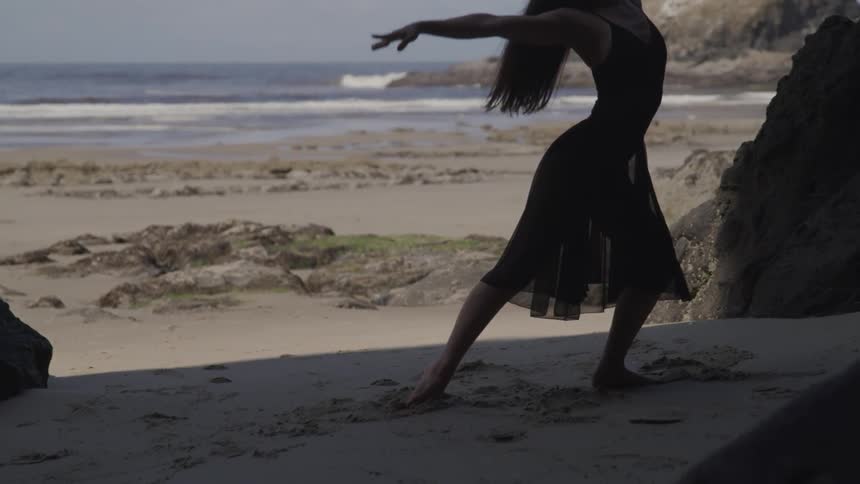 A woman in a black shawl dancing on the beach