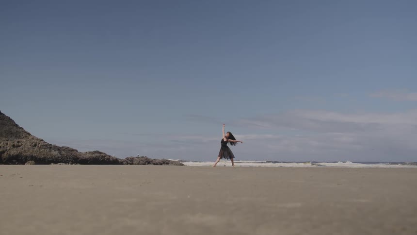 Asian woman in black dress dances on the sand beach next to the sea