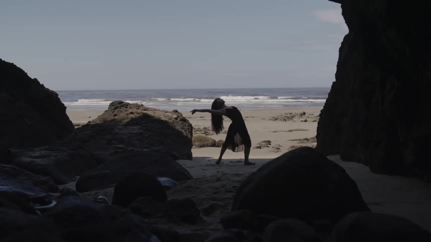 A woman in a black shawl dancing on the beach