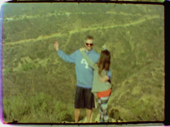 A man and woman pose and kiss with the hollywood sign in the background