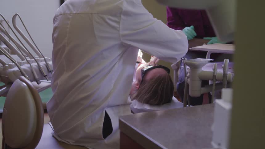 A dentist in a white coat and dental assistant in scrubs are working on a patient