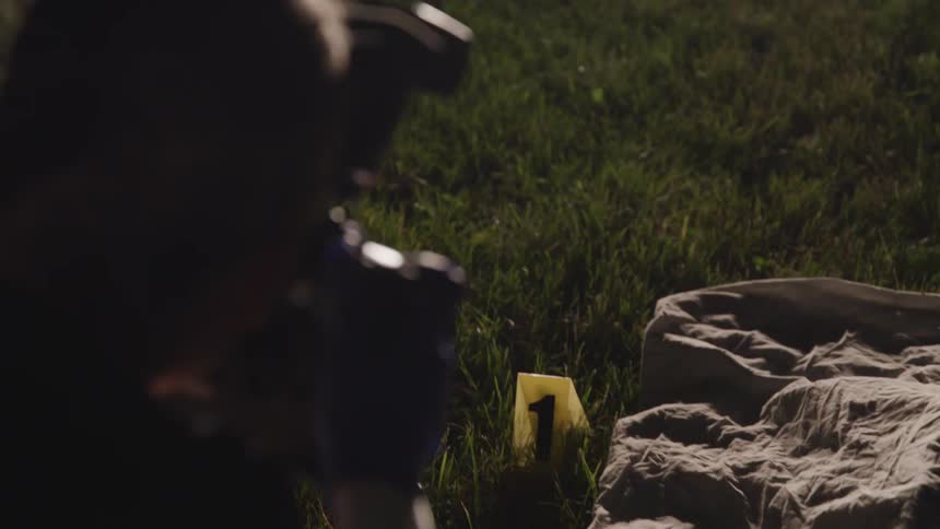 A woman takes a photograph of a crime scene outside at night