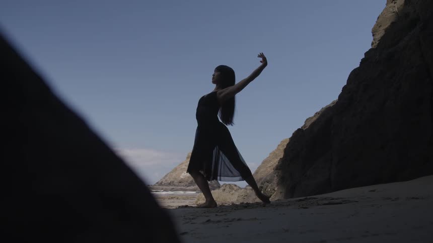 A woman moves into different dance poses while standing on a beach