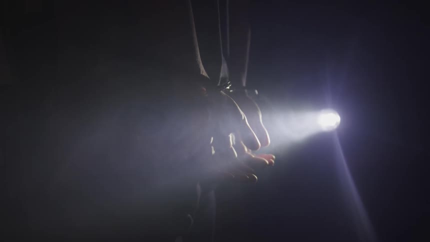 A handcuffed person standing in a dark location with only their cuffed wrists illuminated by light