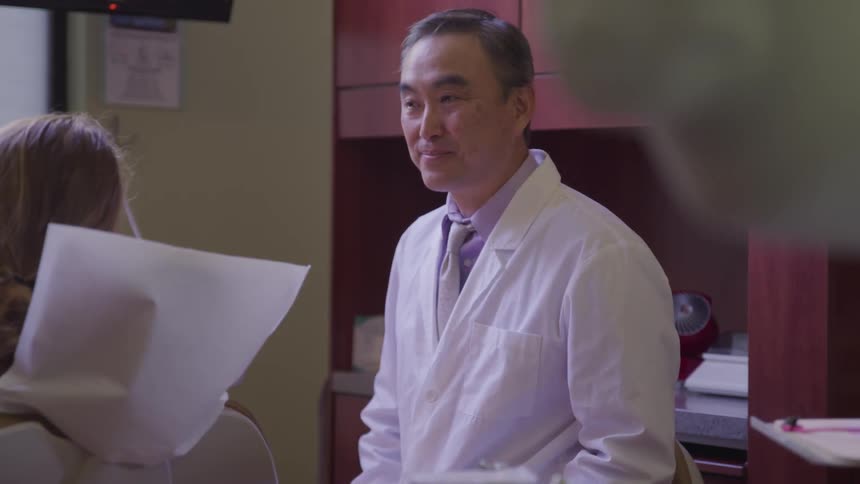 A doctor nods as he talks to a young girl in his office