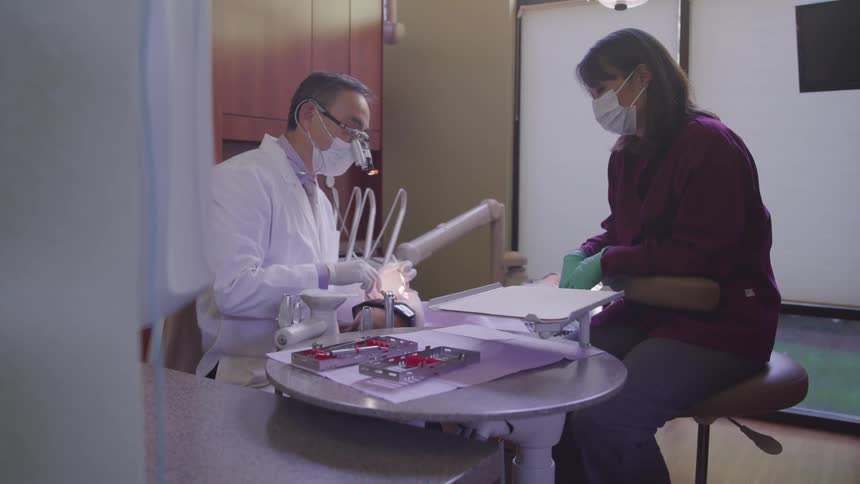 A dentist and assistant works on a patient in an office