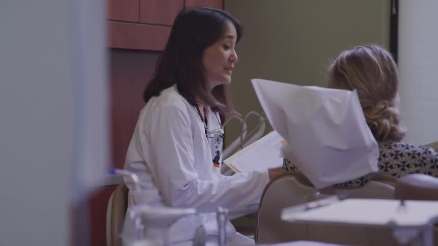 A doctor holds a folder of papers and shows them to a patient