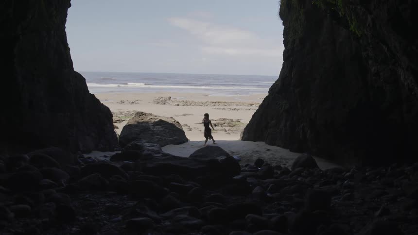 A female gracefully dances within a large cave that opens outwards towards the beach