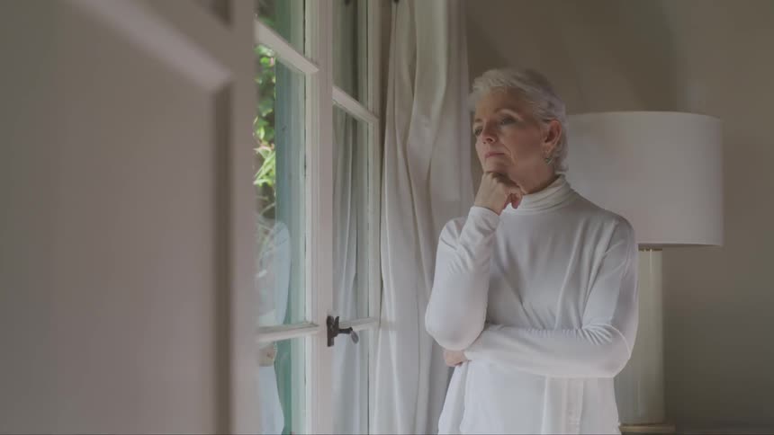 A woman stands next to a window and looks outside