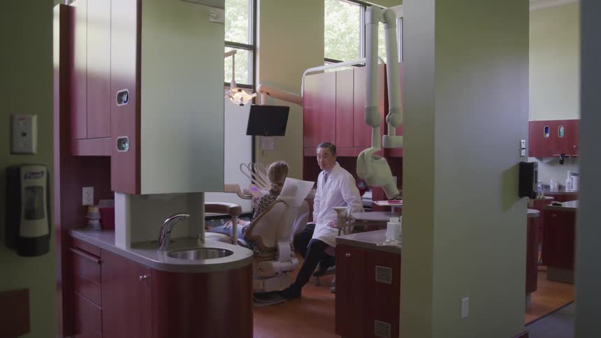 A dentist talks to a patient while she sits in the dental chair