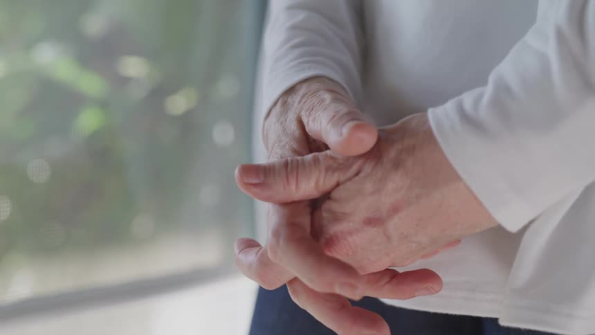 A person stands with their hands clasped in front of them