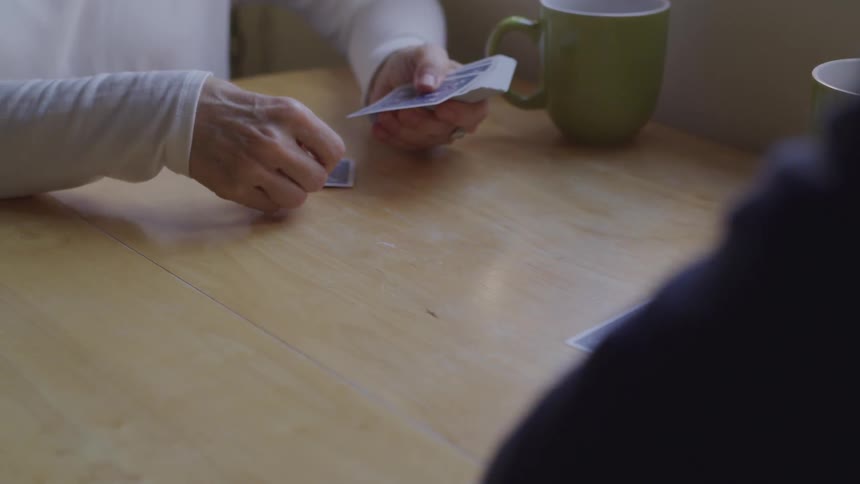 An elderly woman deals cards to another person