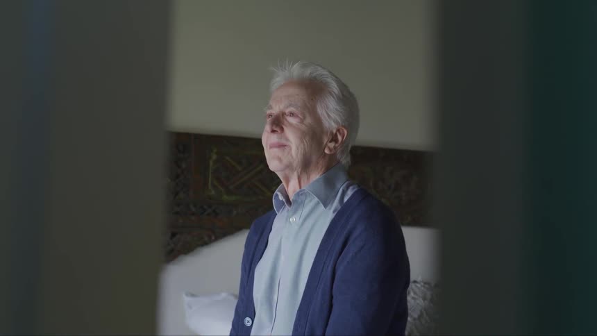 A man smiles sitting in his bedroom