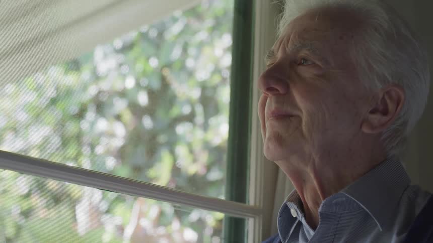 A man smiles as he stares out a window in his house