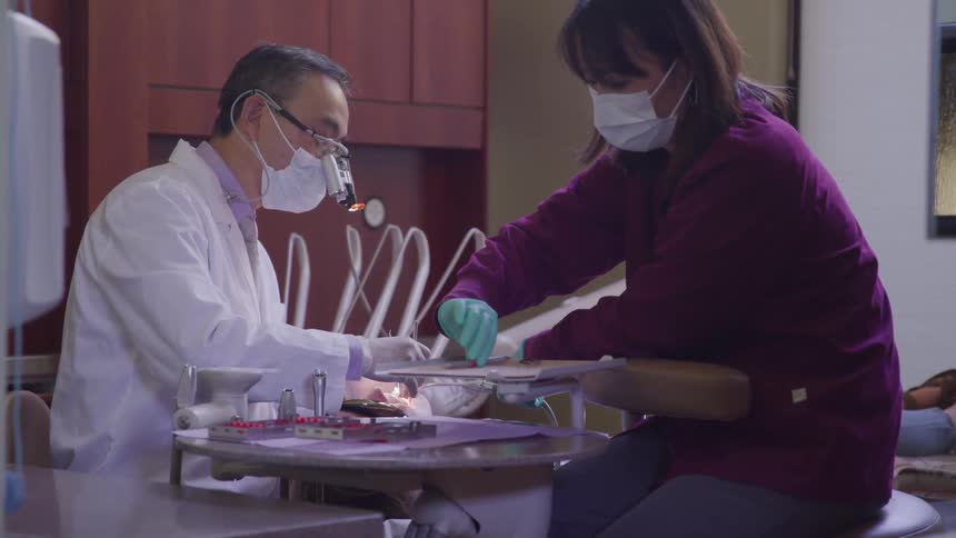 A dentist and assistant do dental work on a patient