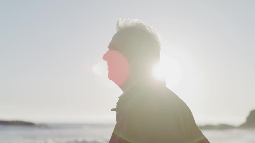 A man stands in profile at the beach on a sunny day