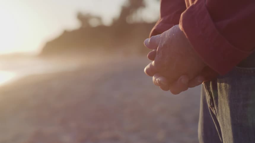A person stands on the beach with their hands held in front of them